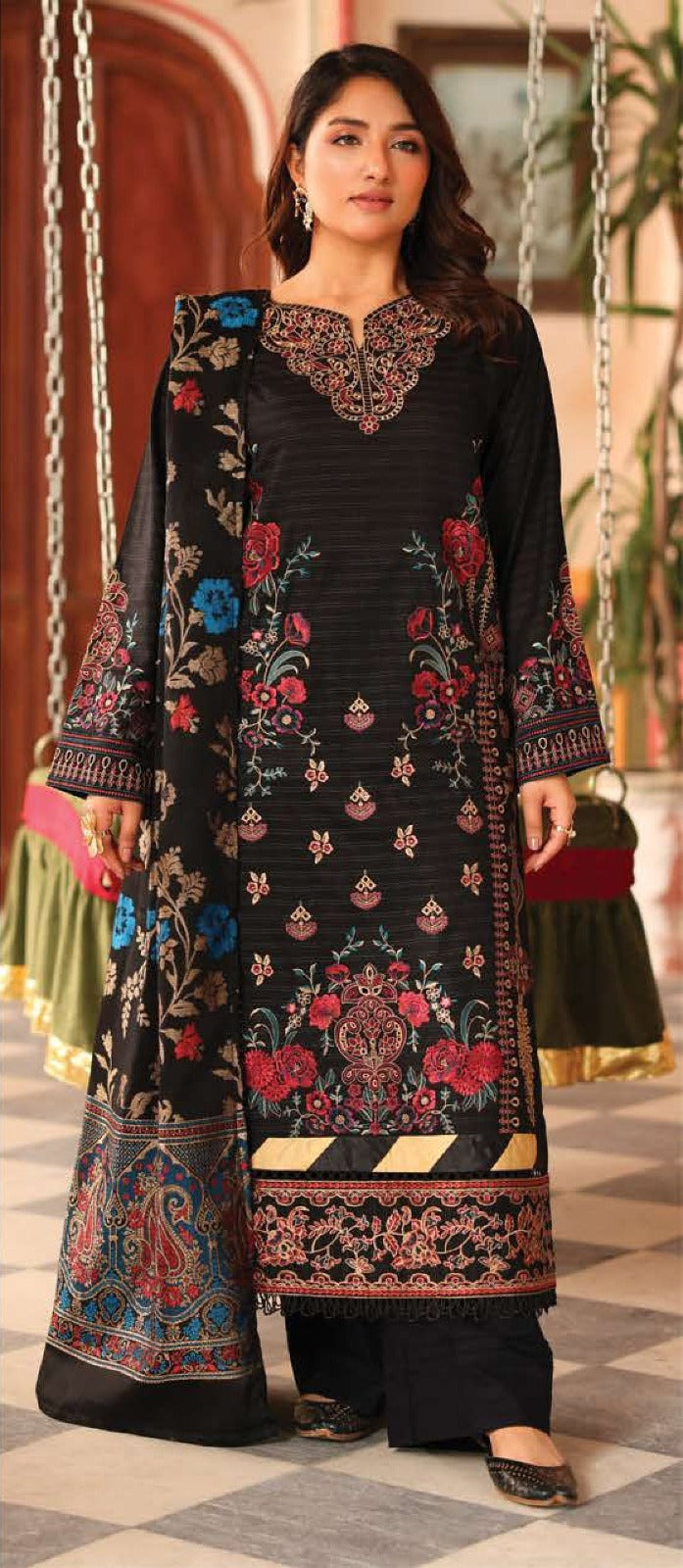 Woman wearing a black embroidered dress with colorful patterns in an indoor setting.