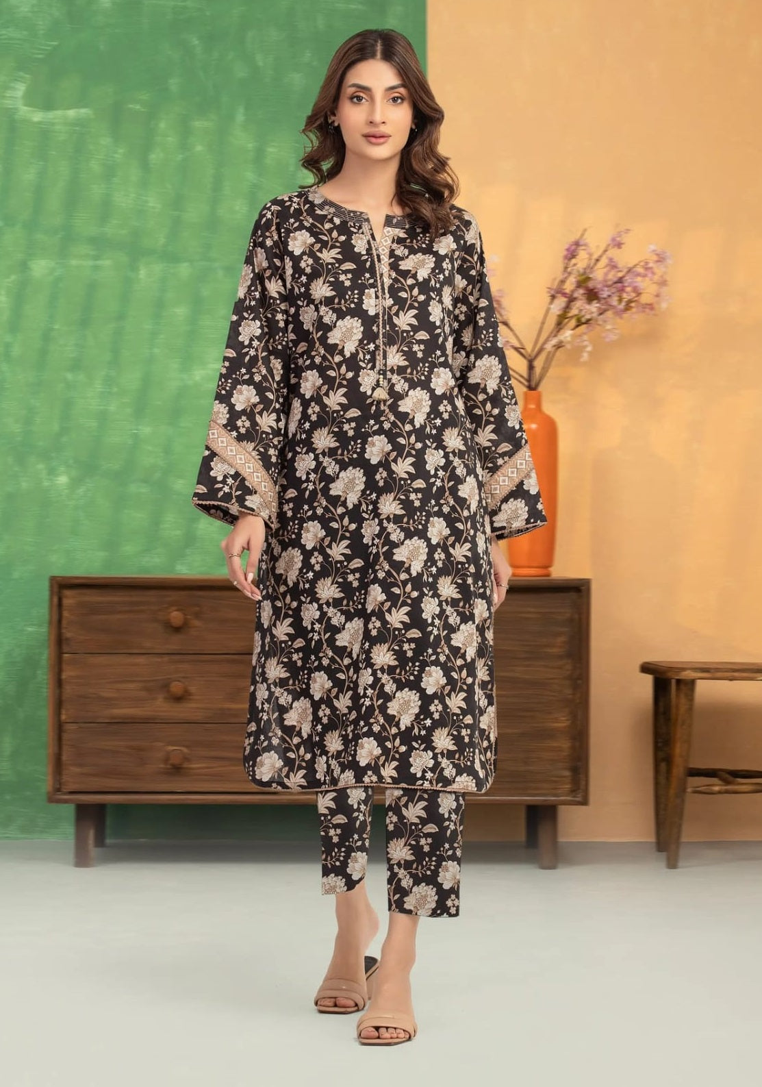 Woman wearing a black floral dress standing in front of a green and beige wall with a wooden cabinet.