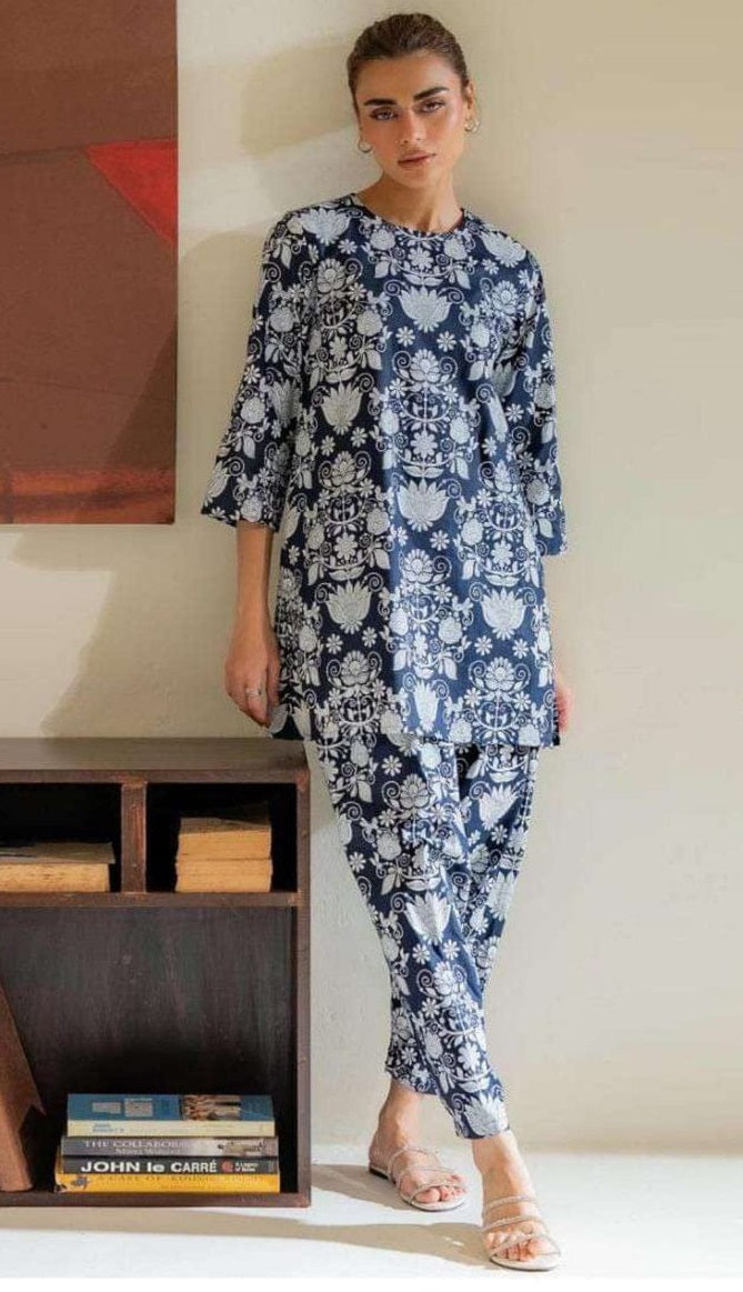 Woman wearing a blue floral outfit standing in a room with a bookshelf and abstract painting.