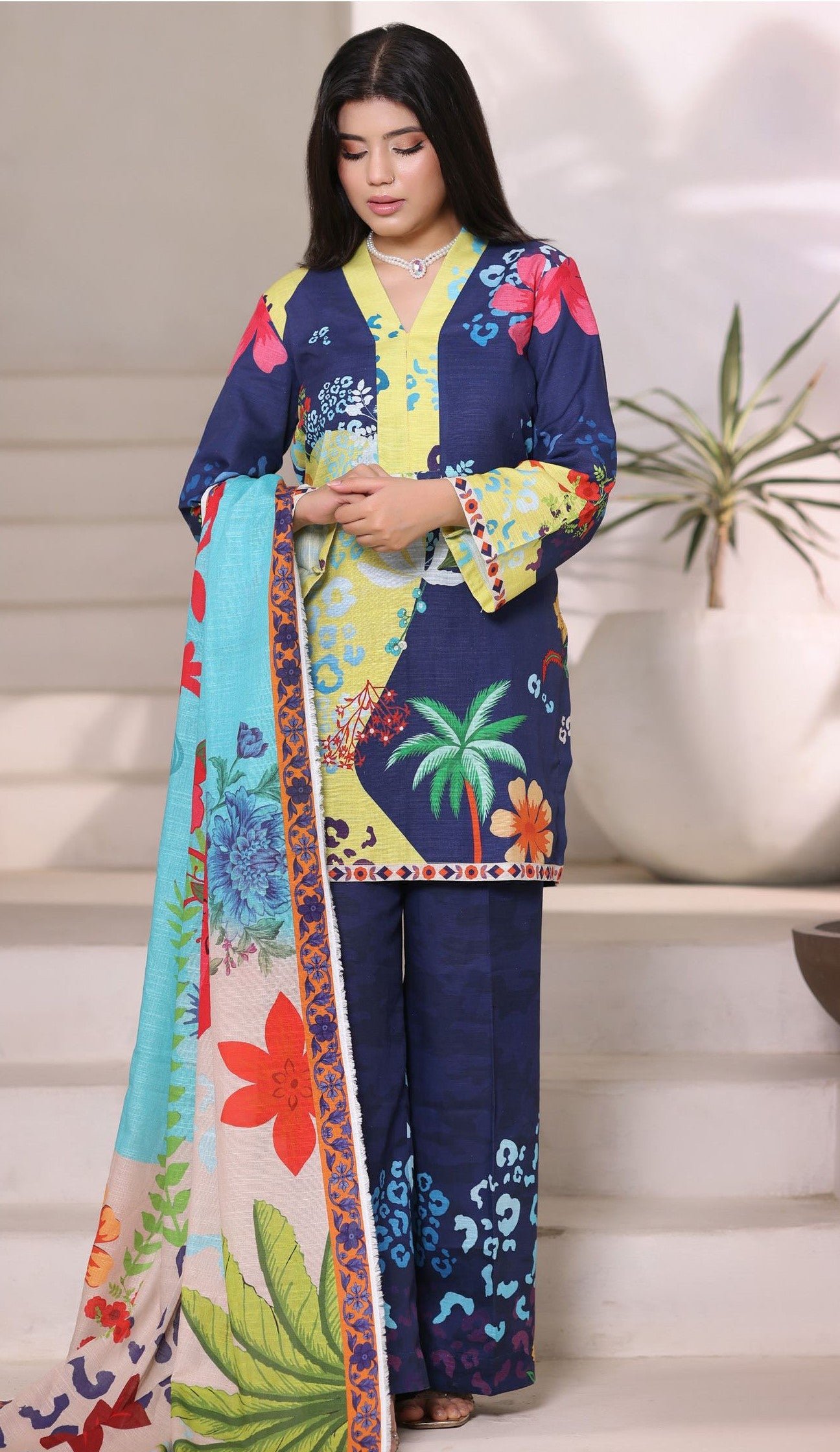 Woman wearing a colorful floral outfit with a patterned scarf indoors.