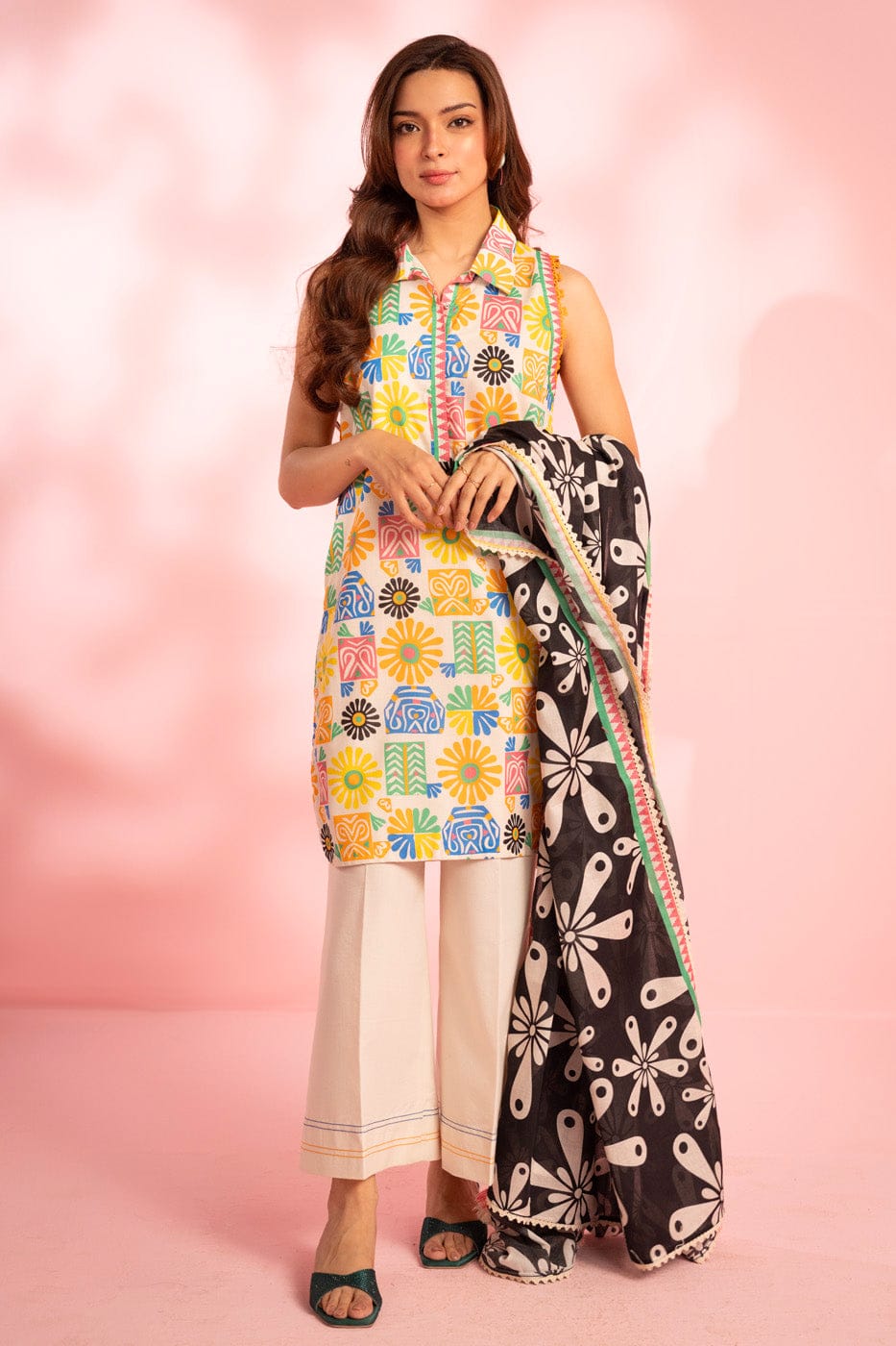 Woman wearing a colorful patterned outfit with a black and white scarf on a pink background