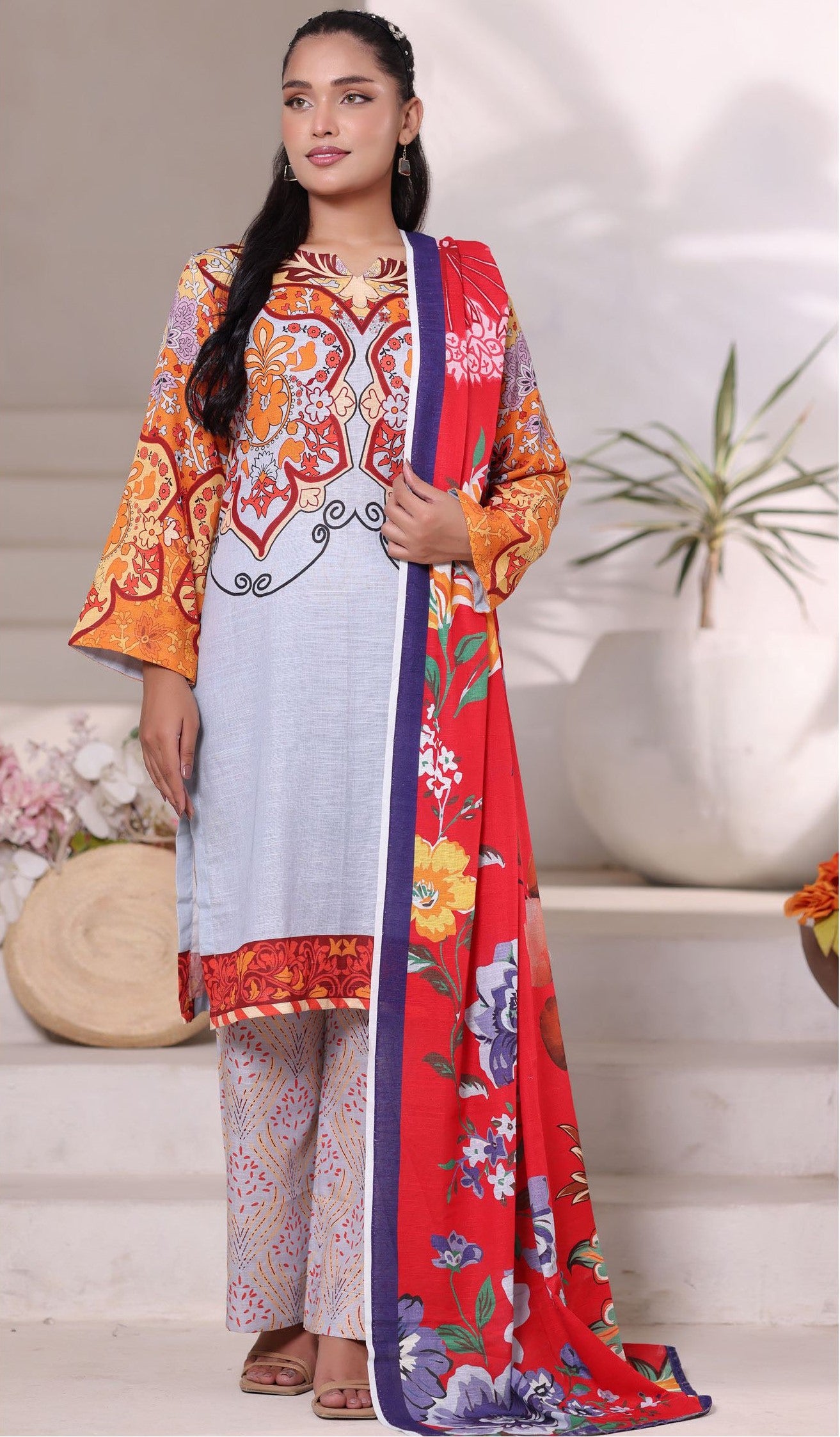 Woman wearing a colorful traditional outfit with a red dupatta in a home setting.