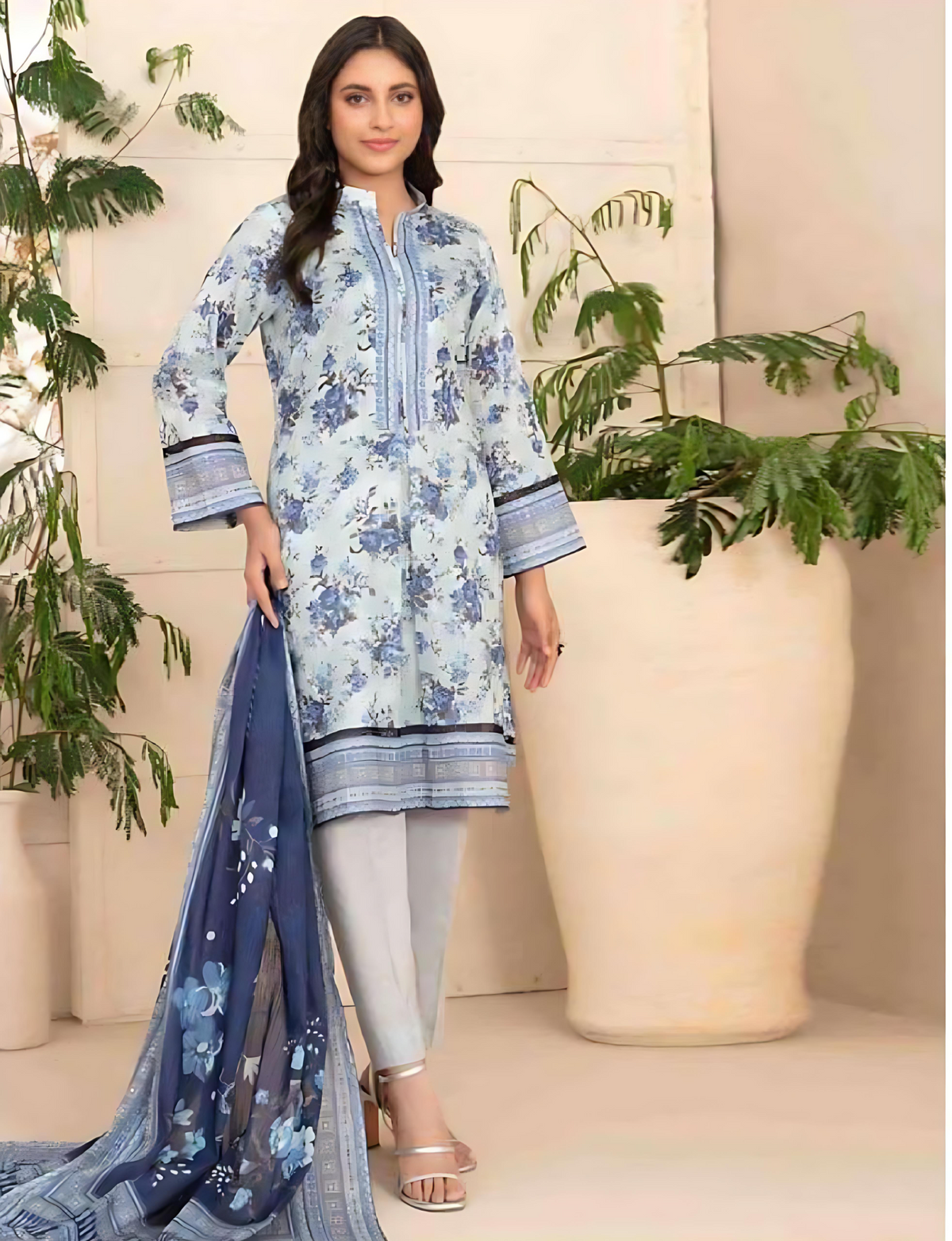 Woman wearing a floral dress with a blue dupatta in a decorated indoor setting.