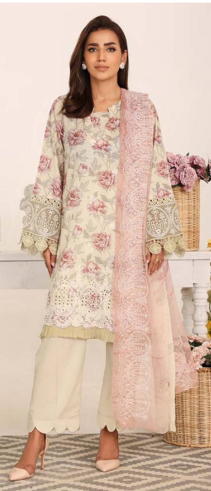 Woman wearing a floral embroidered outfit with a pink dupatta, standing in a decorated room.