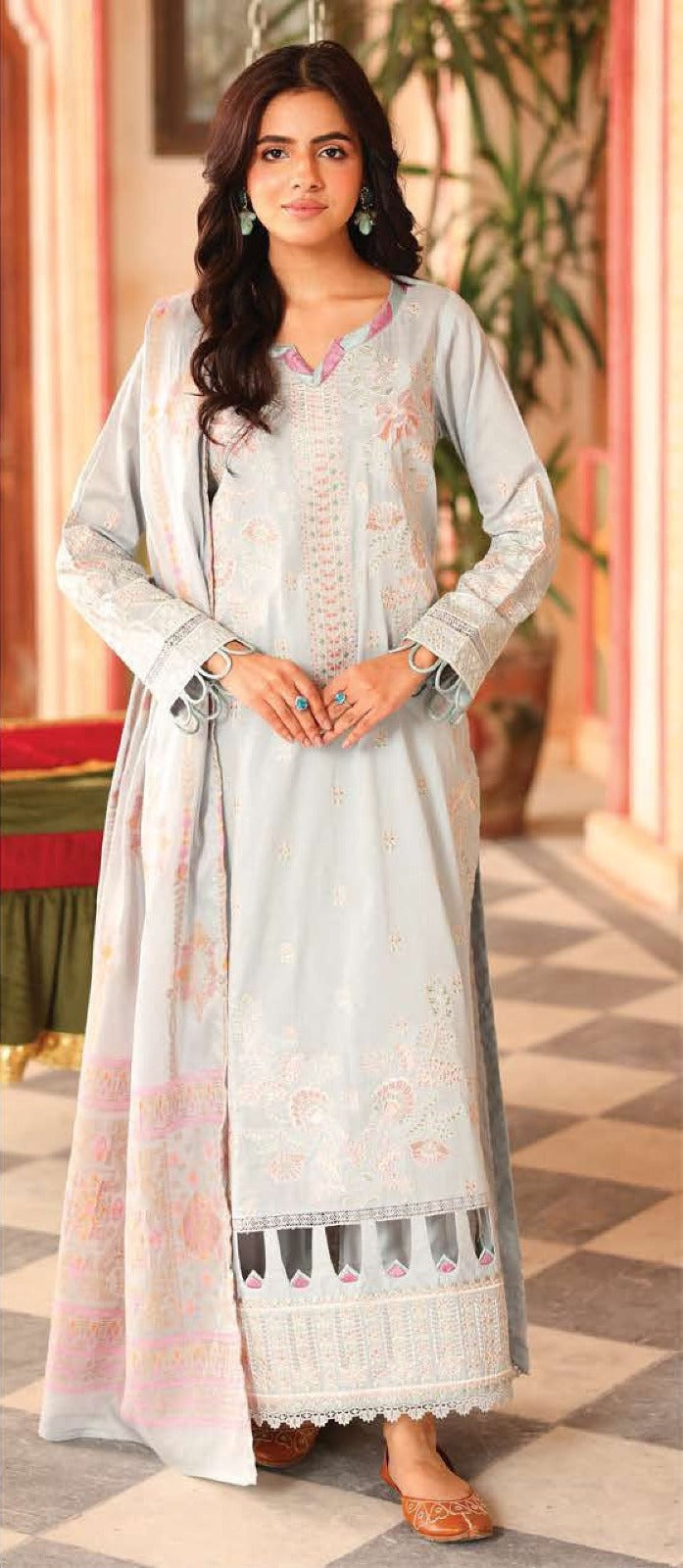 Woman wearing a light-colored traditional outfit with floral patterns in an indoor setting.