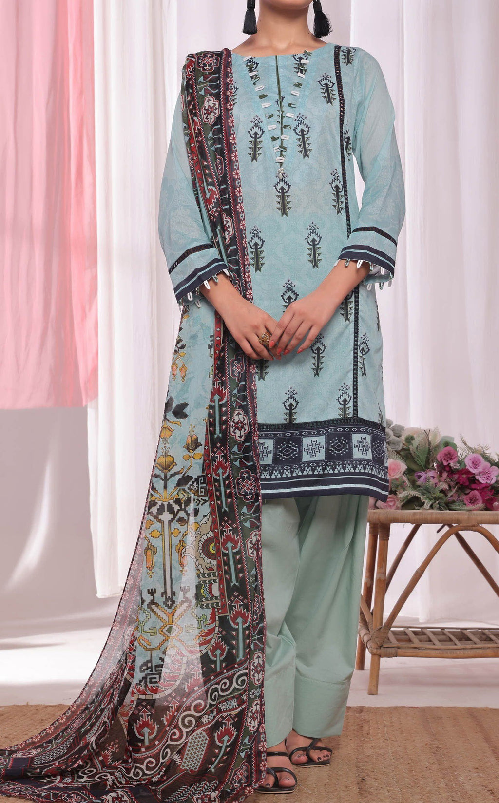 Woman wearing a light blue printed outfit with a patterned dupatta against a white curtain background.