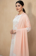 Woman wearing a light pink dupatta over a white outfit against a beige background