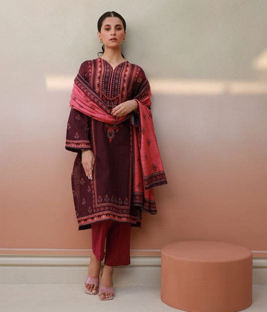 Woman wearing a maroon and pink traditional outfit against a light pink wall.