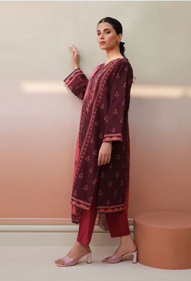 Woman wearing a maroon and pink traditional outfit against a beige wall.