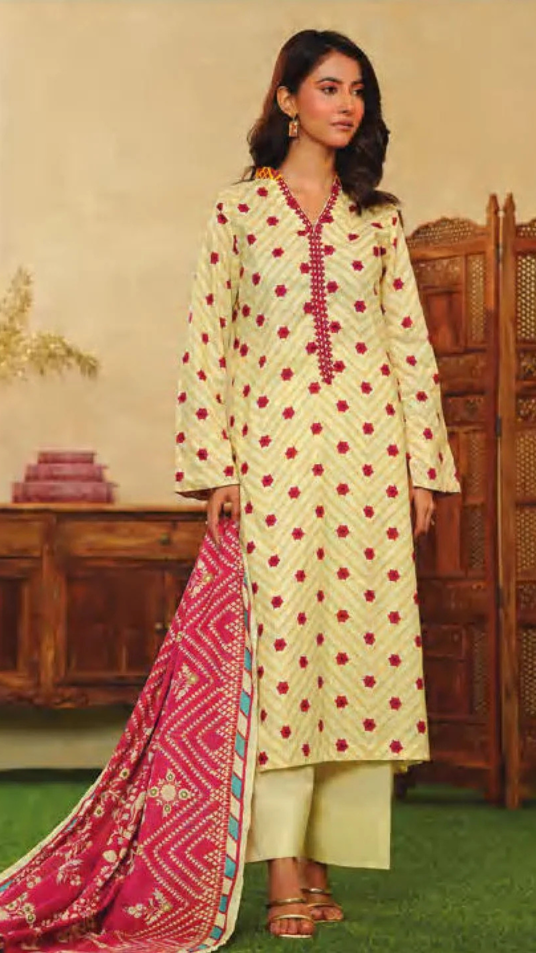 Woman wearing a mor e bagh light yellow kurta with red floral patterns and a pink dupatta in a decorated room.