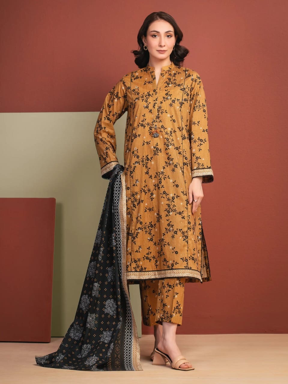 Woman wearing a mustard yellow floral outfit with a black dupatta against a red and beige background