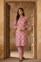 Woman wearing a pink floral outfit standing in a doorway.