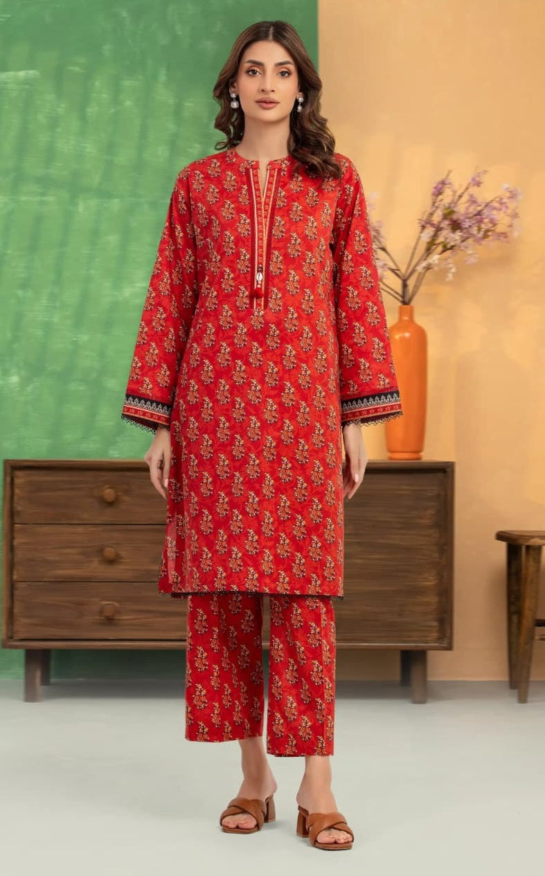 Woman wearing a red floral outfit standing in a room with a green wall and wooden furniture.