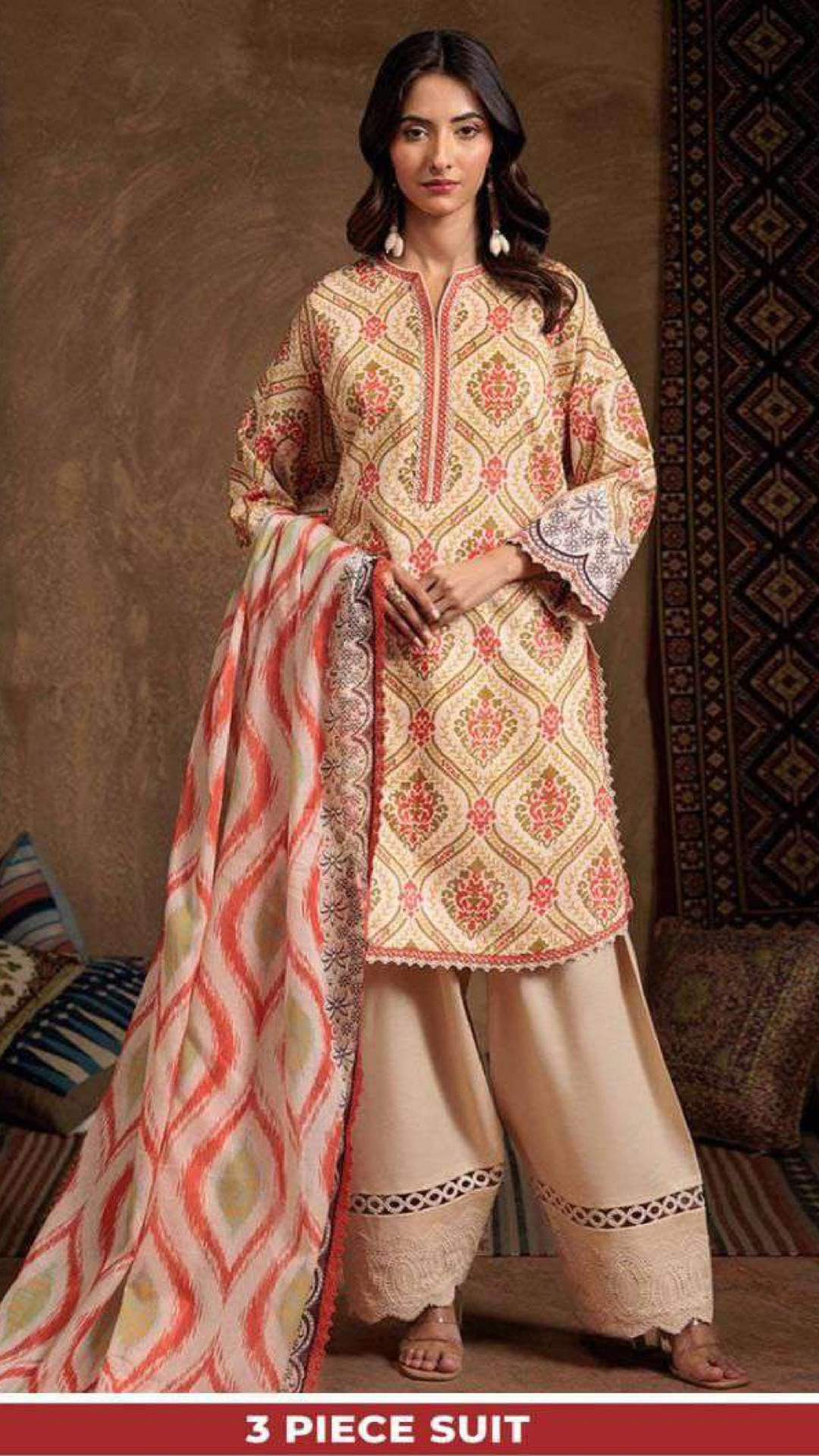 Woman wearing a three-piece suit with a patterned top and beige pants, holding a matching dupatta.