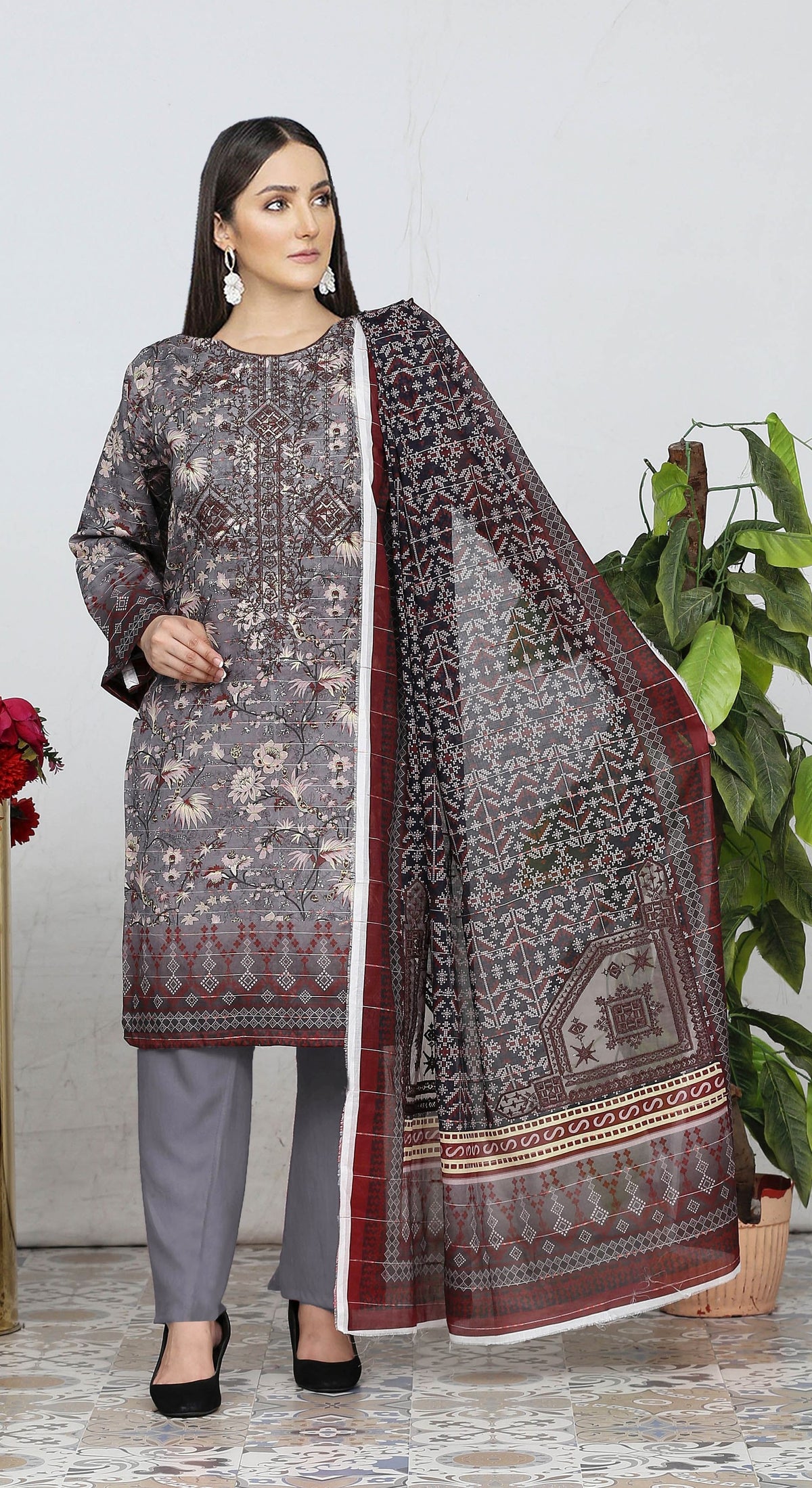 Woman wearing a traditional outfit with a patterned dupatta, standing indoors with a plant in the background.