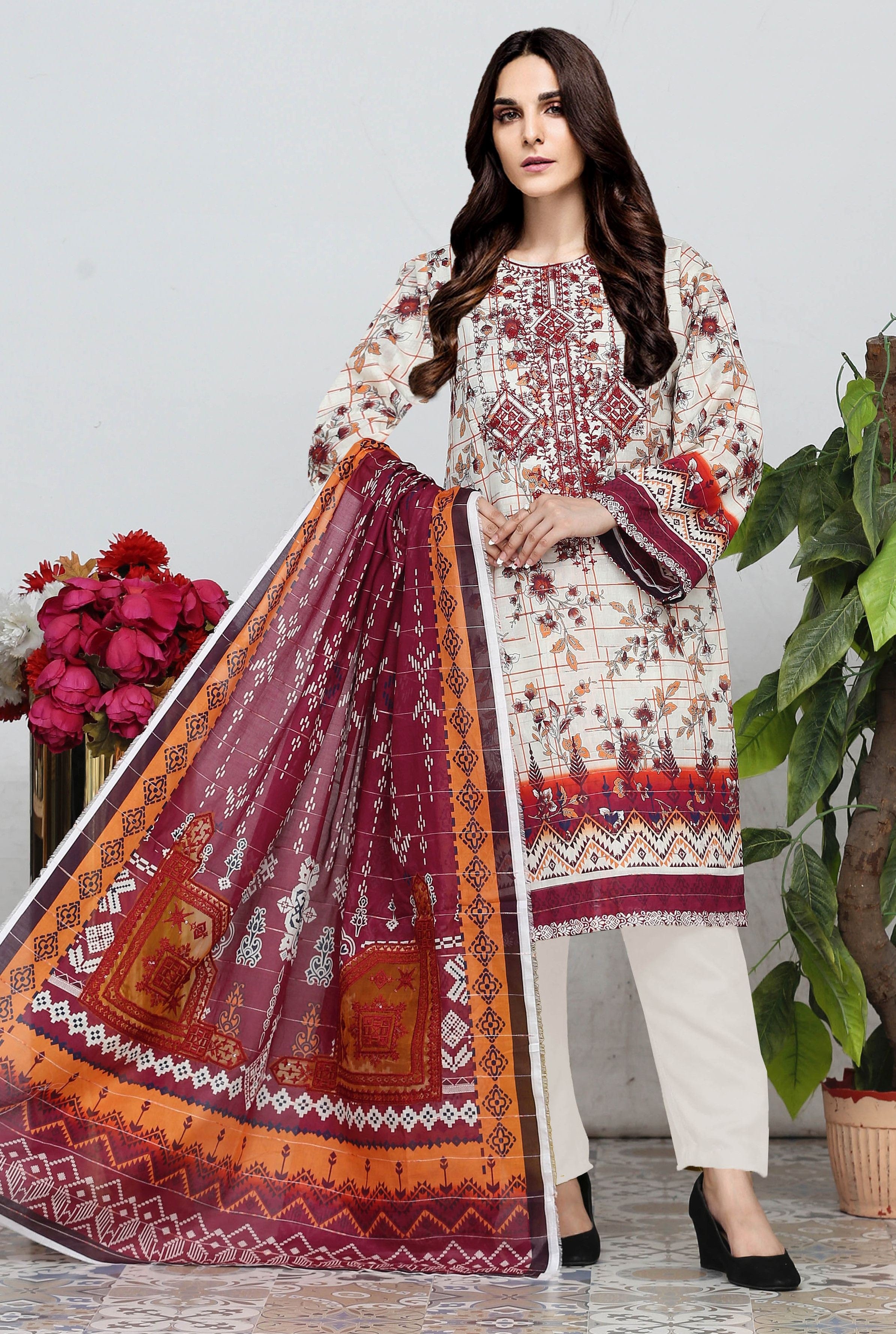 Woman wearing a traditional outfit with a patterned dupatta, standing next to flowers and a plant.