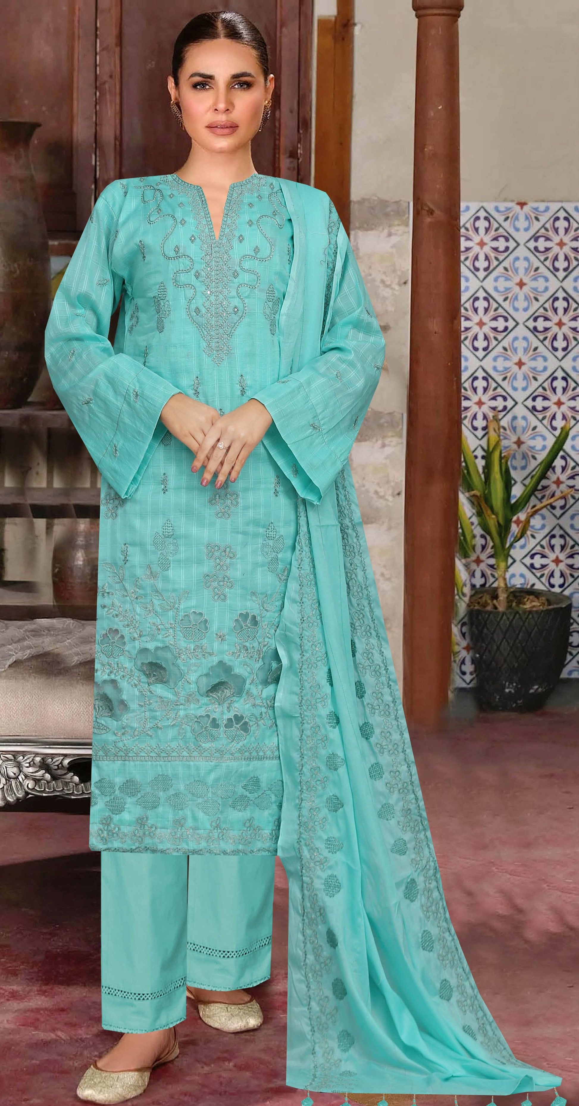 Woman wearing a turquoise embroidered outfit in an indoor setting with decorative elements.