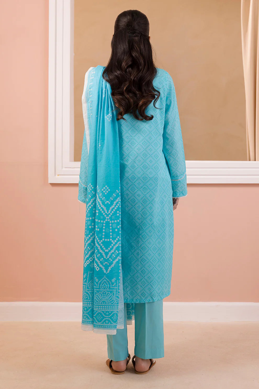 Woman wearing a turquoise traditional outfit with a matching dupatta against a beige wall.