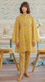 Woman wearing a yellow floral outfit in a room with wooden furniture and decorative elements.