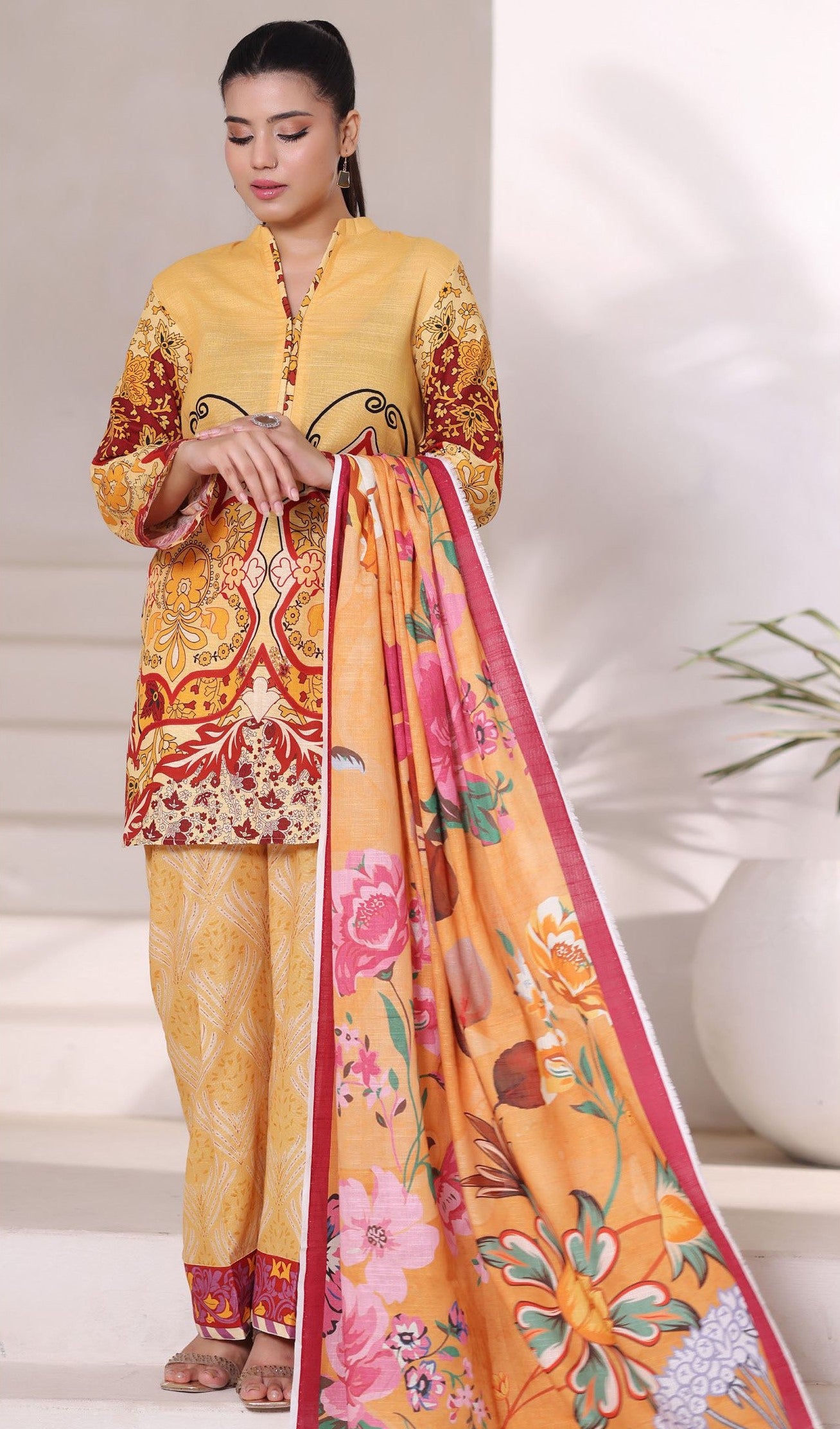Woman wearing a yellow traditional outfit with floral patterns, holding a matching dupatta.