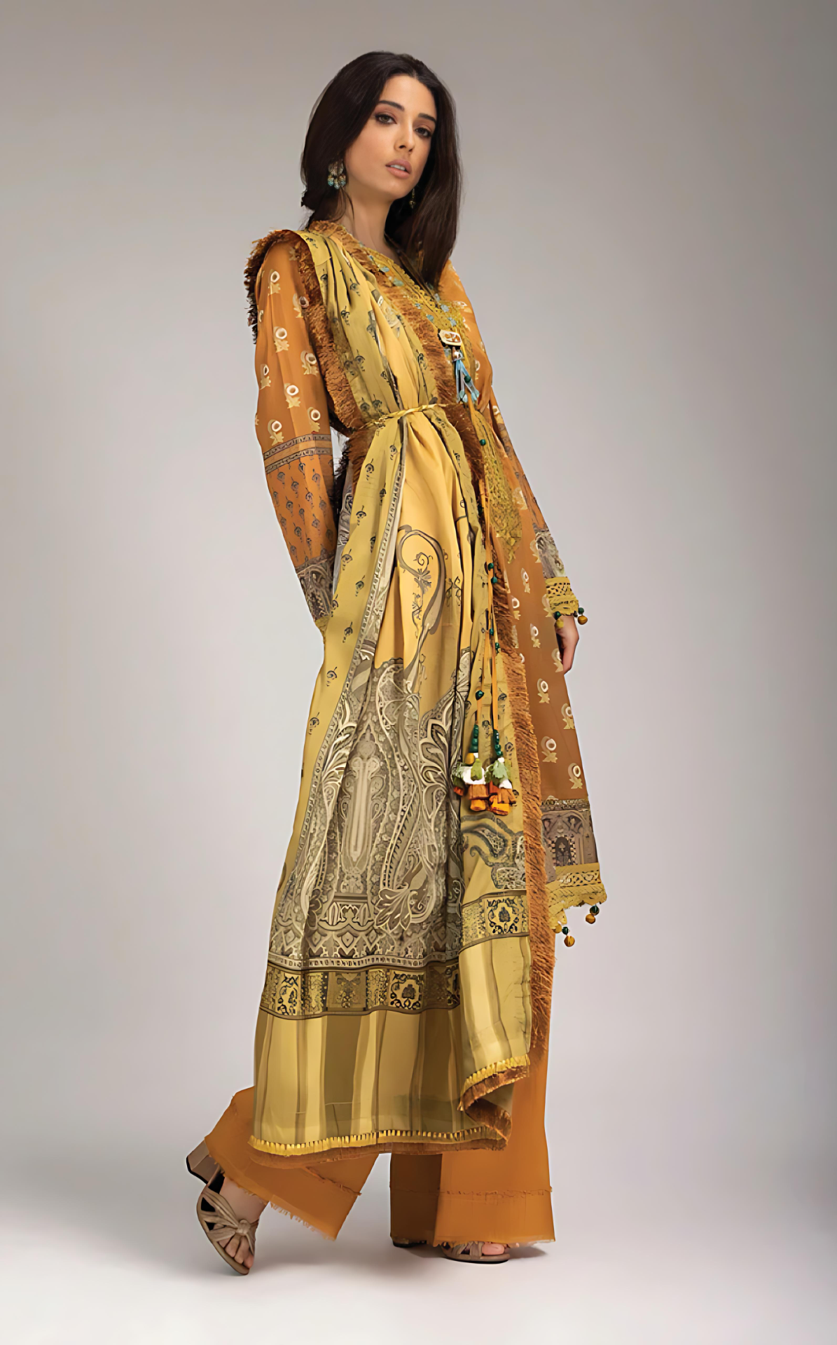 Woman wearing sobia nazir long, patterned yellow dress with a matching dupatta on a gray backgrounda 