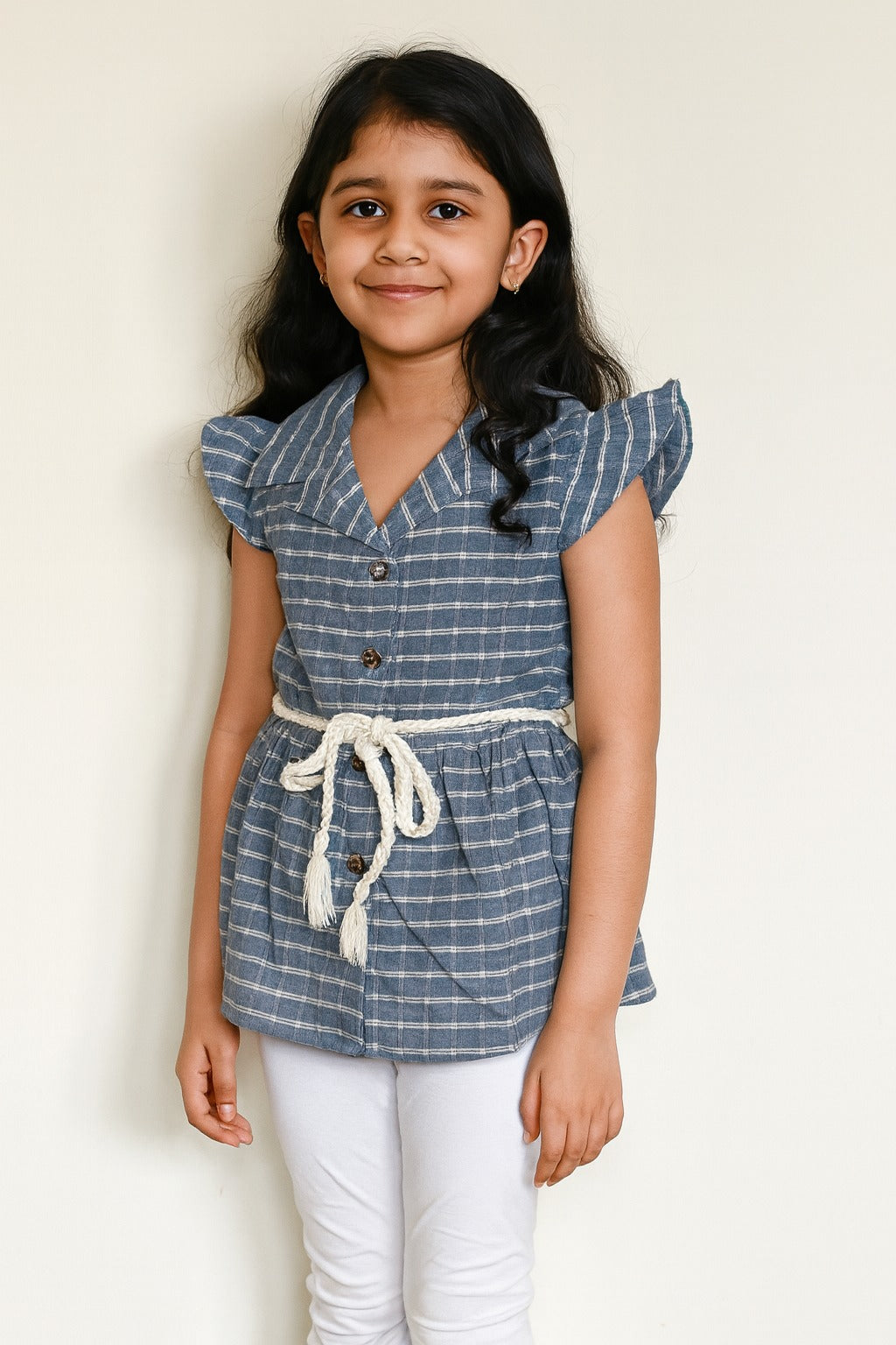Young girl wearing a blue checkered top with white buttons against a plain background