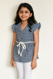 Young girl wearing a blue checkered top with white buttons against a plain background
