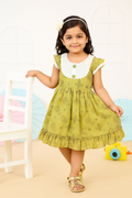 Young girl wearing a green dress with white collar and buttons, standing in a room.