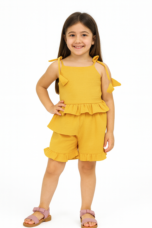 Young girl wearing a yellow outfit with ruffled top and shorts on a white background