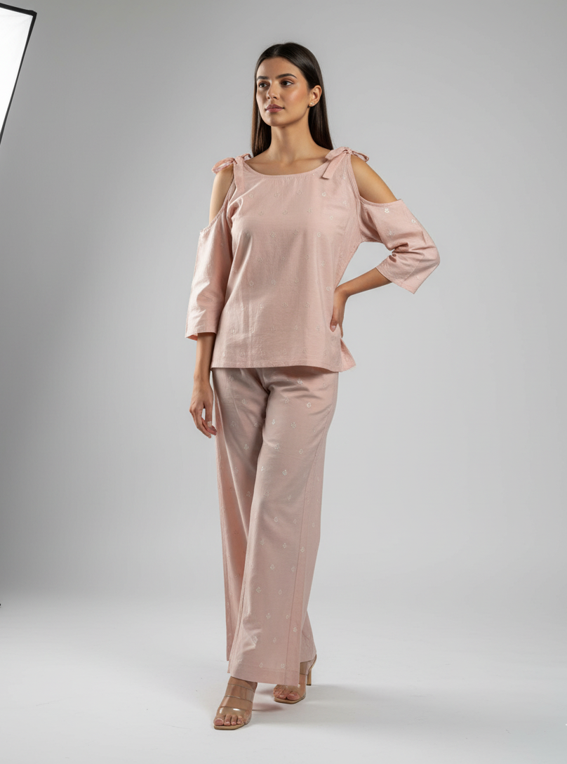 Woman wearing a pink outfit with cold-shoulder top and pants on a gray background