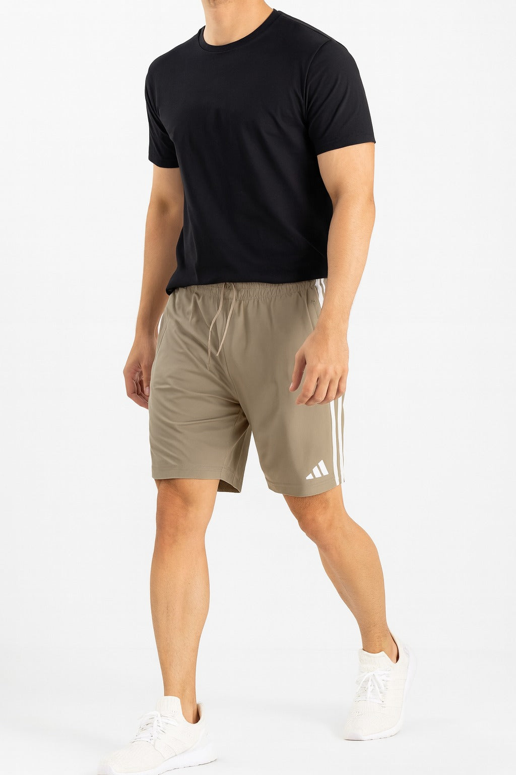 Person wearing a black t-shirt and beige Adidas shorts on a white background