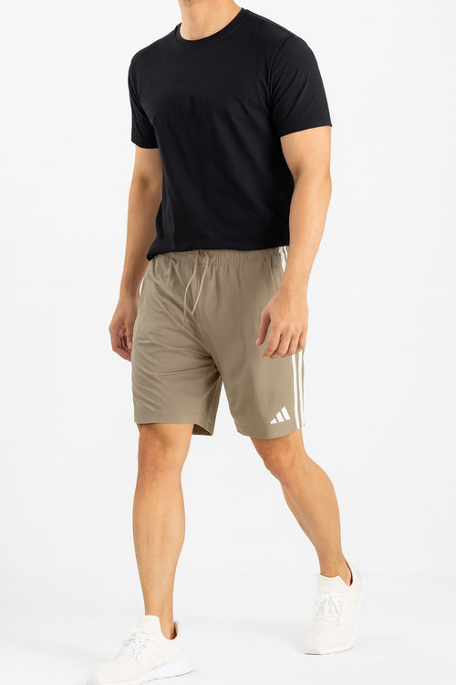 Person wearing a black t-shirt and beige Adidas shorts on a white background