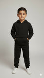 Child wearing a black hoodie and pants on a plain background