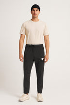 Man wearing a beige t-shirt and black pants with a logo on a white background