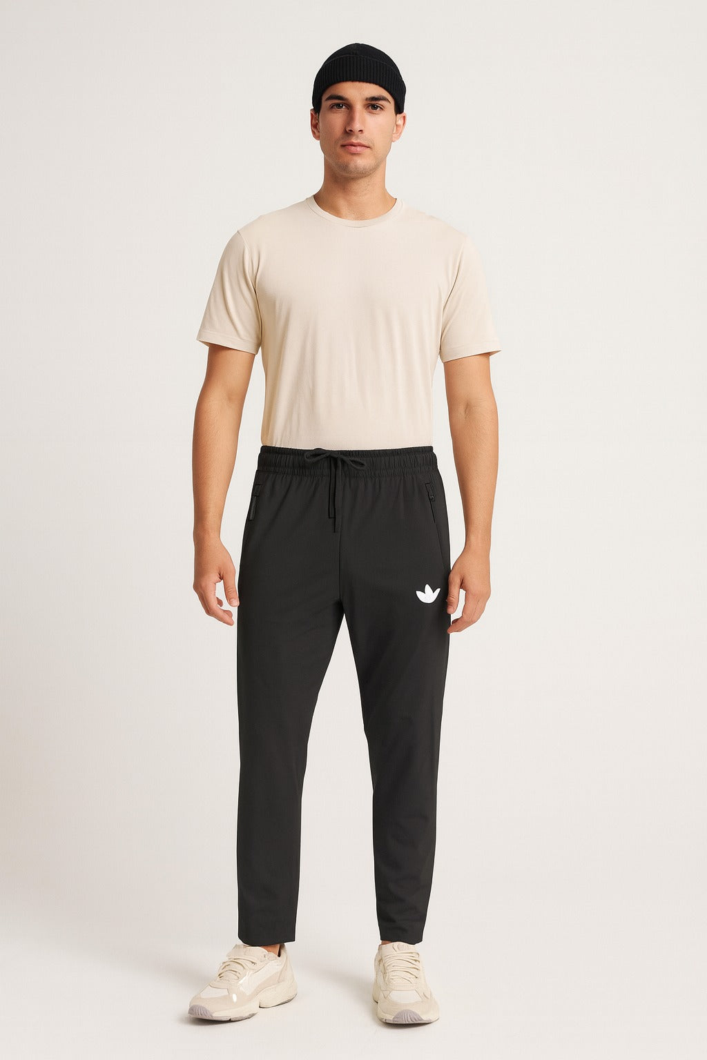 Man wearing a beige t-shirt and black pants with a logo on a white background