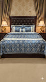 Decorative bedspread with blue and white patterns on a bed in a bedroom setting.