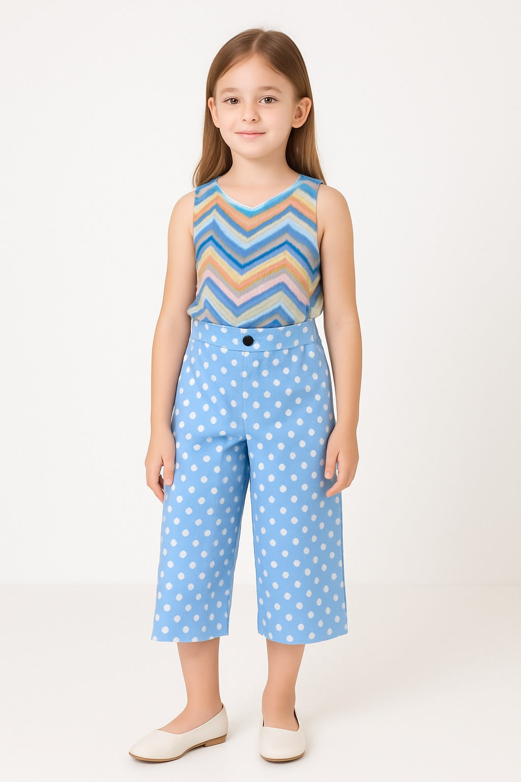Young girl wearing a sleeveless top with a striped pattern and blue polka dot pants on a white background