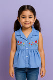 Young girl wearing a blue sleeveless shirt with floral embroidery against a purple background