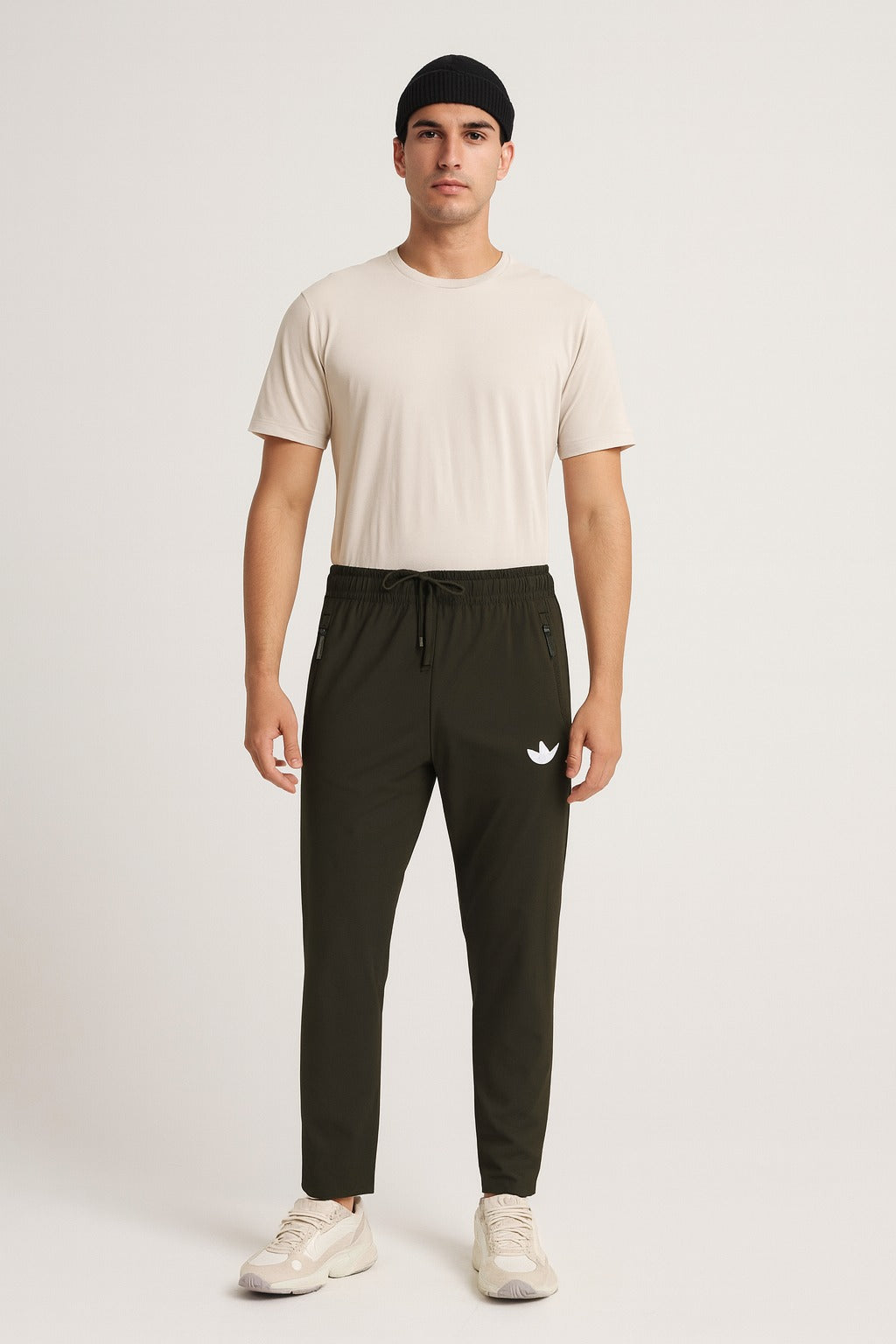 Man wearing a beige t-shirt and dark green pants with a logo on a white background