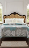 Bed with floral comforter and tufted headboard in a room with large windows.