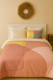Bed with geometric patterned bedding against a beige wall with a decorative wreath.