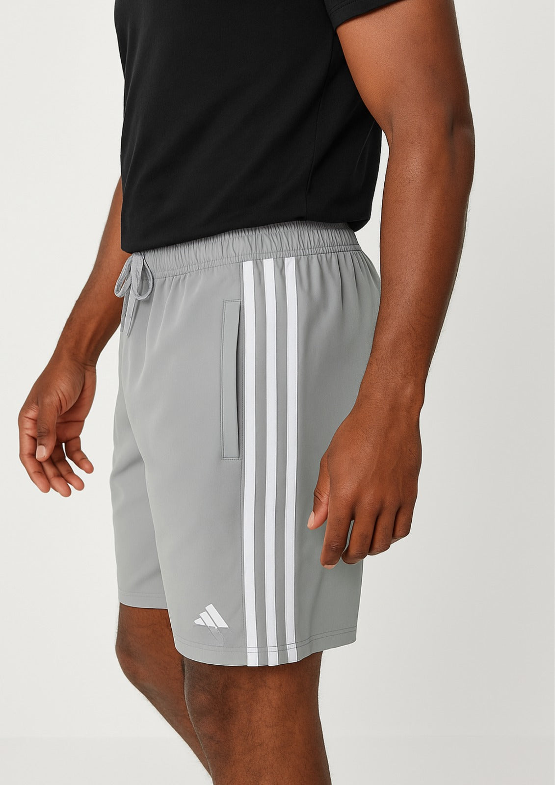Person wearing gray Adidas shorts with white stripes on a plain background