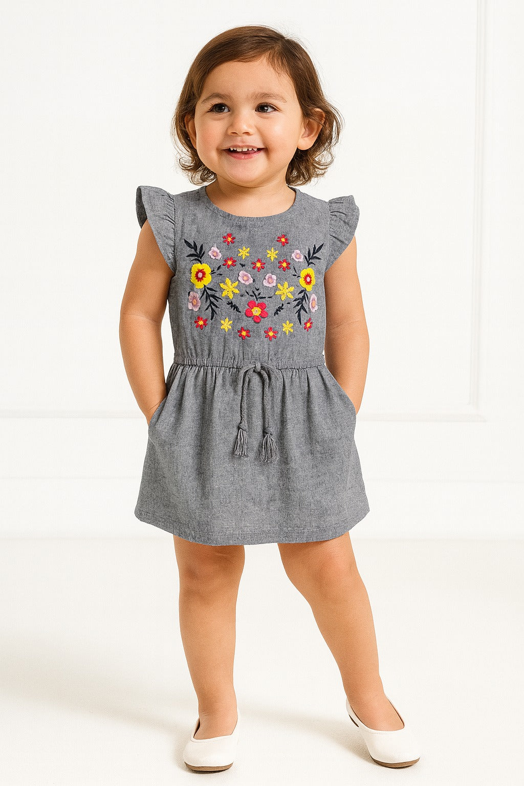 Child wearing a gray dress with floral embroidery on a white background