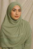 Woman wearing a green hijab and outfit against a beige background