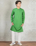 Man wearing a green kurta with white pants against a textured wall.