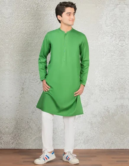 Man wearing a green kurta with white pants against a textured wall.
