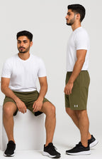 Two men wearing green shorts and white t-shirts, one sitting and one standing, on a white background.