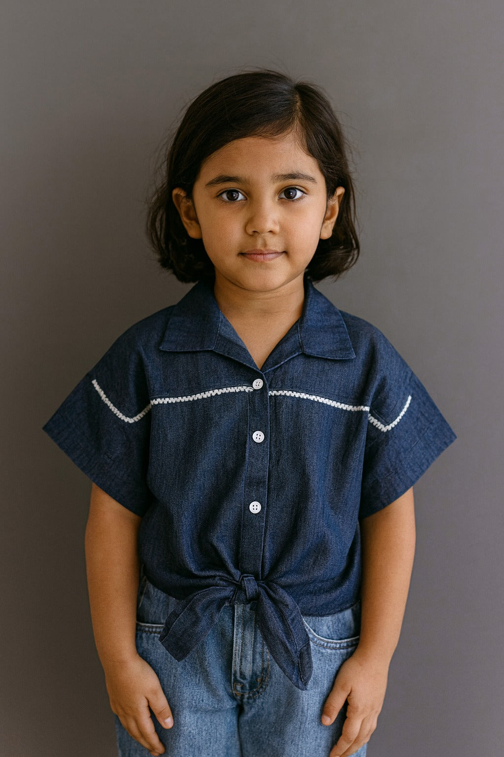 Child wearing a navy blue shirt with white trim against a gray background