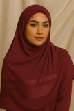 Woman wearing a maroon hijab against a beige background