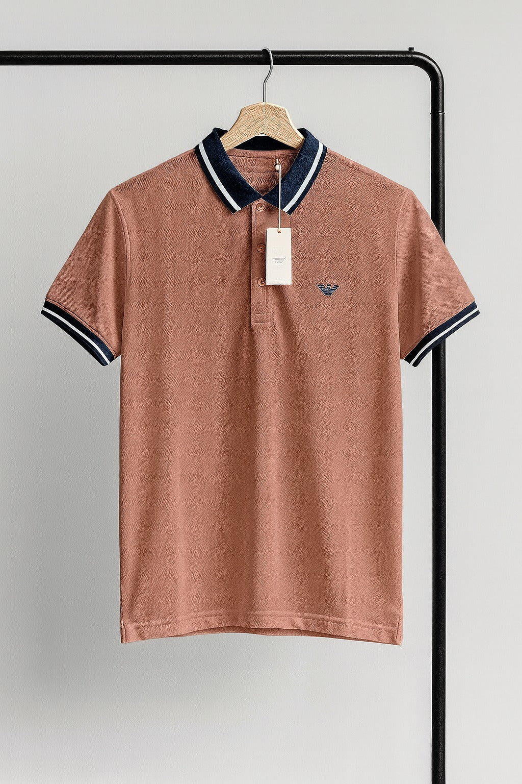 peach brown polo shirt with black and white trim on a hanger against a gray background